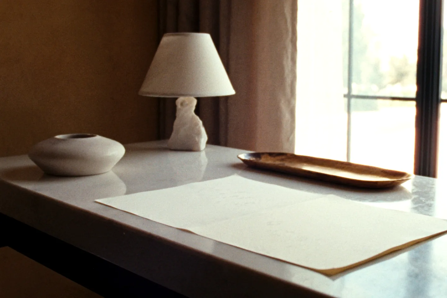 A sunlit limestone writing desk with a stone lamp and blank cream stationery by a window.